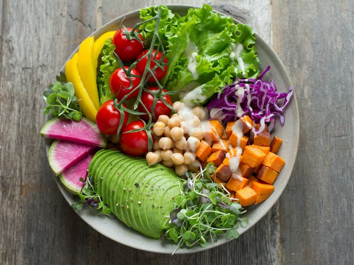 A bowl of salad with avocado, tomatoes, chickpeas and leaves