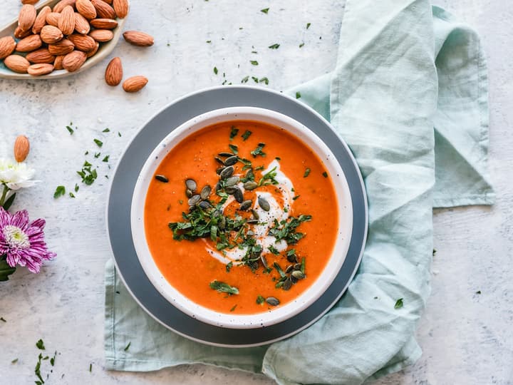 A bowl of tomato soup topped with herbs and seeds